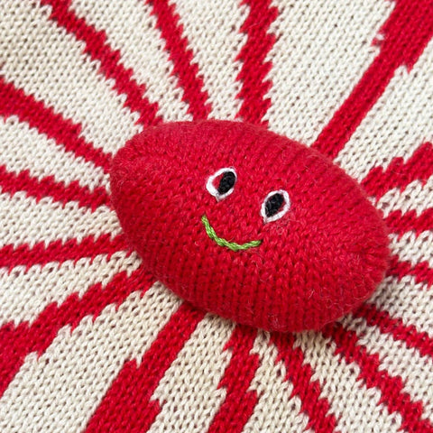 Red knitted ball with a face on a red and white striped background