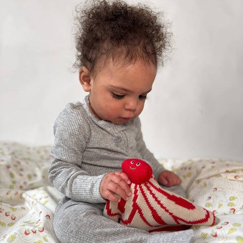 Baby holding a red and white knitted toy on a patterned blanket