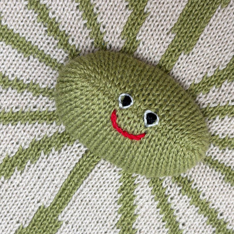 Knitted green character with a red mouth and black eyes on a striped fabric background