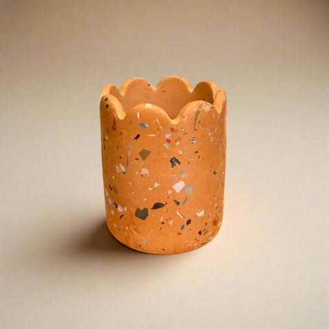 Terracotta-colored candle holder with speckled pattern on a cardboard surface