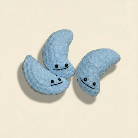 Three blue moon-shaped plush toys with faces on a wooden floor.