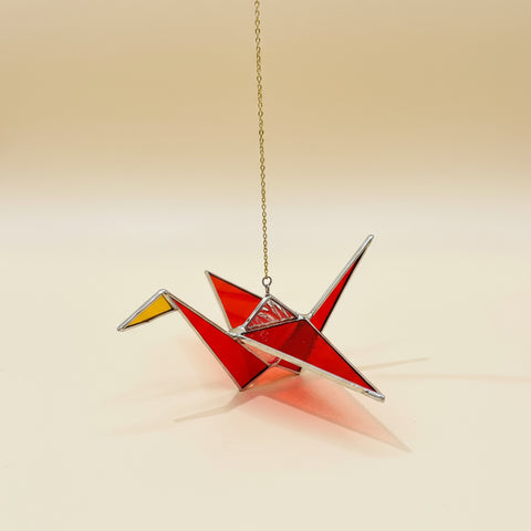 Red stained glass origami crane hanging on a chain against a blurred indoor background