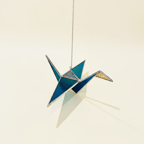 Decorative stained glass crane on a wooden surface with a store shelf in the background