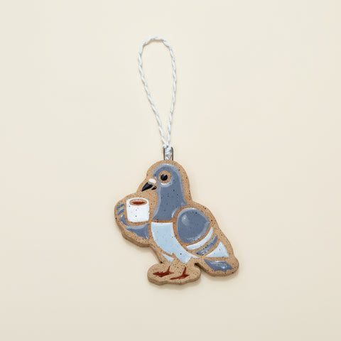 Decorative pigeon ornament holding a cup on a wooden surface