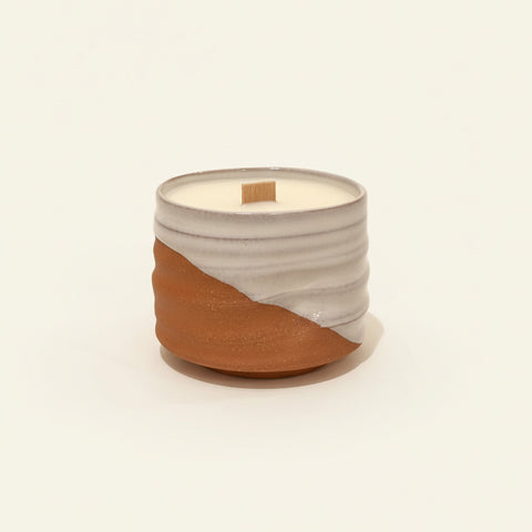 Ceramic candle with wick on a wooden surface.