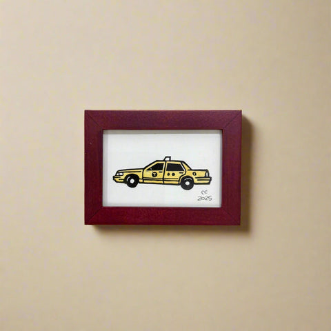 Framed artwork of a yellow taxi on a wooden surface