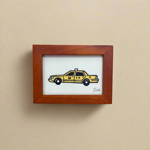 Small framed picture of a yellow taxi on a wooden surface