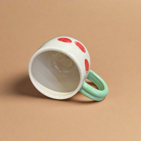 White cup with red spots and a green handle on a cardboard surface