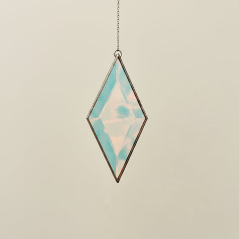 Diamond-shaped pendant with iridescent finish on a chain against a neutral background