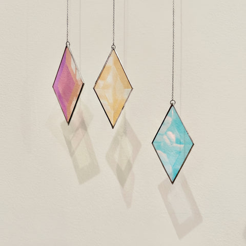 Three diamond-shaped stained glass panels hanging against a light gray wall.