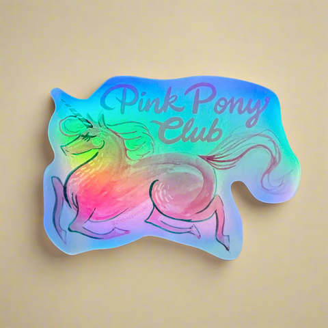 Holographic sticker of a pink pony with 'Pink Pony Club' text on a tan surface