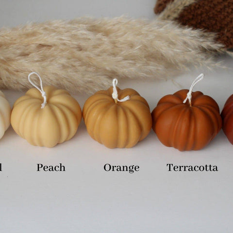 Row of pumpkin candles in different colors with labels on a textured surface