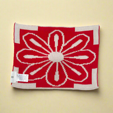 Red and beige knitted blanket with a floral pattern on a white background