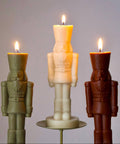 Three nutcracker-shaped candles on stands with a plain background