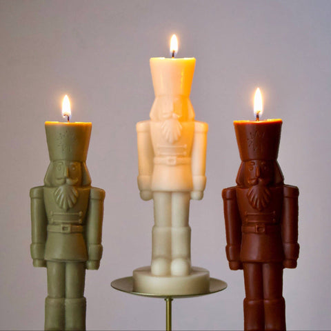Three nutcracker-shaped candles on stands with a plain background