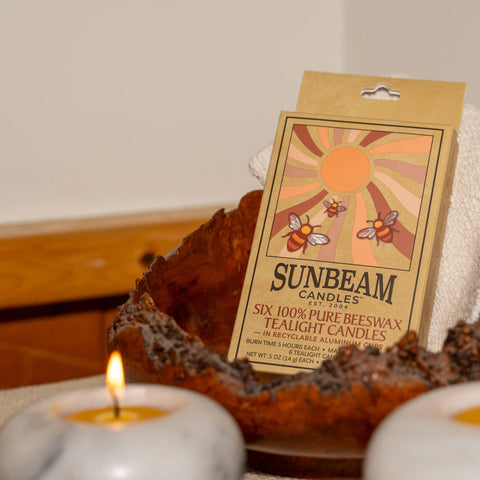 Sunbeam candles packaging with two lit candles on a wooden surface.