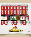 Decorative tea towel with a New York City-themed design featuring a yellow taxi, red building, and Christmas tree.