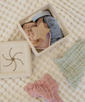Collection of baby toys including a star-shaped wooden toy, pink knitted item, and green textured item on a textured surface.