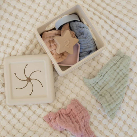 Collection of baby toys including a star-shaped wooden toy, pink knitted item, and green textured item on a textured surface.