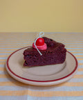 Miniature slice of chocolate cake with cherry on a striped tablecloth