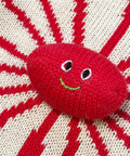 Red knitted ball with a face on a red and white striped background