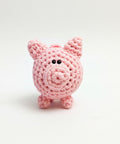 A small pink crocheted pig toy held in a person's hand against a plain white background.