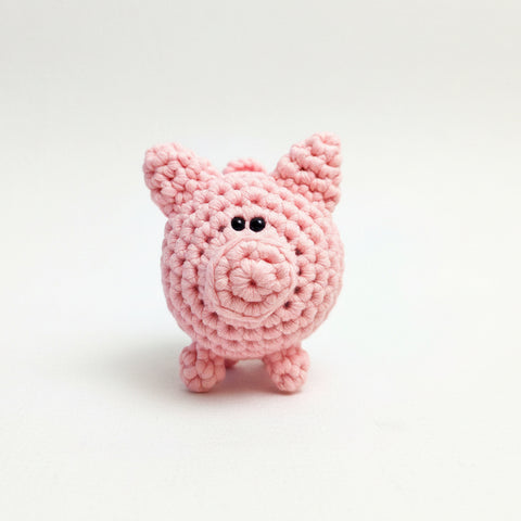 A small pink crocheted pig toy held in a person's hand against a plain white background.