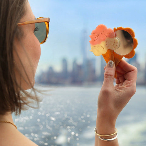 Person holding a compact mirror with floral design by a waterfront