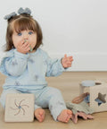 Child in a light blue outfit playing with wooden blocks on a wooden floor.