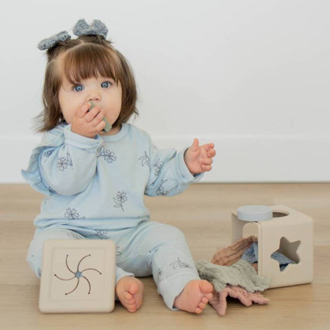 Child in a light blue outfit playing with wooden blocks on a wooden floor.
