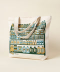 Tote bag with a colorful design leaning against a white brick wall.