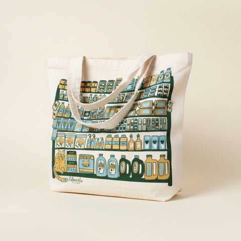 Tote bag with a colorful design leaning against a white brick wall.