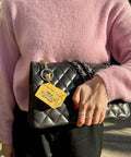 Person wearing a pink sweater holding a black quilted handbag with a yellow tag.
