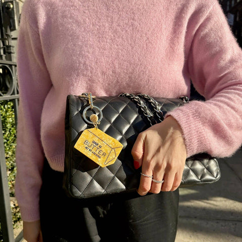 Person wearing a pink sweater holding a black quilted handbag with a yellow tag.