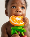 Baby holding an orange teething toy with a neutral background