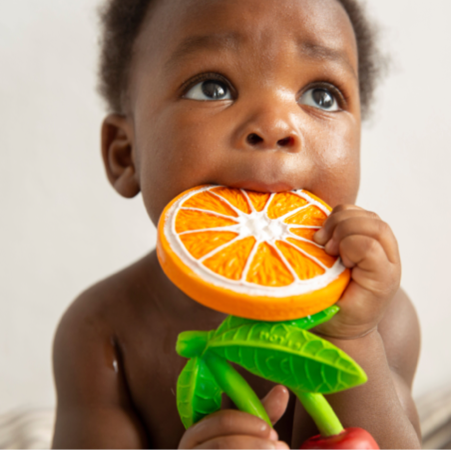 Baby holding an orange teething toy with a neutral background