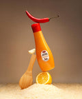 Mustard bottle with a red cap, wooden spoon, and lemon on a sandy surface with a brown background