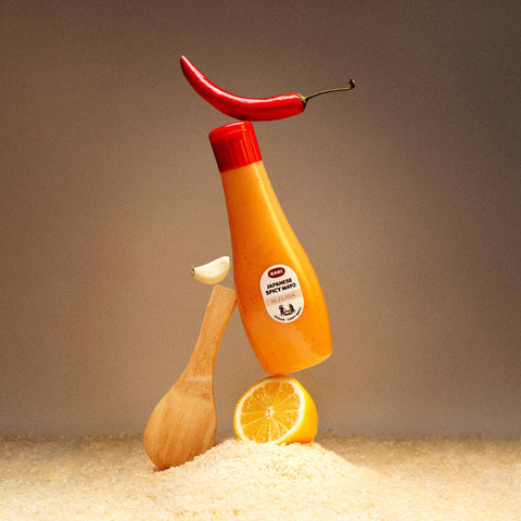 Mustard bottle with a red cap, wooden spoon, and lemon on a sandy surface with a brown background