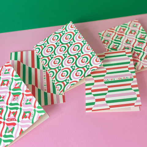 Set of Christmas-themed greeting cards with geometric patterns on a pink surface.
