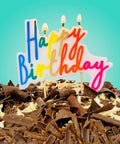 Chocolate birthday cake with colorful 'Happy Birthday' topper against a teal background