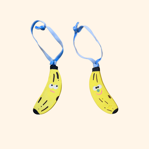 Two cartoon-style banana-shaped ornaments with blue ribbon on a beige background