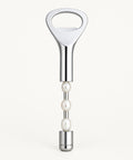A silver metal bottle opener with a pearl-bead handle lies on a beige drawstring bag against a dark blue background.