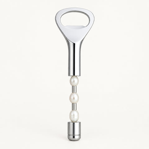 A silver metal bottle opener with a pearl-bead handle lies on a beige drawstring bag against a dark blue background.
