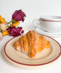 Croissant on a plate with a cup and saucer, and dried flowers on a white background