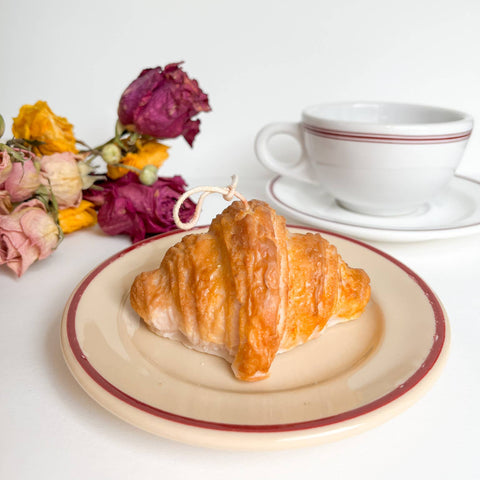Croissant on a plate with a cup and saucer, and dried flowers on a white background
