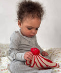 Baby holding a red and white knitted toy on a patterned blanket