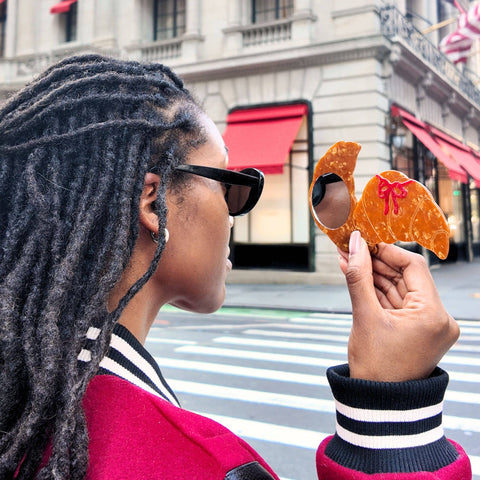 Person holding a croissant shaped mirror on a city street.