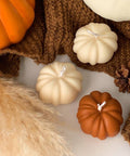 Decorative pumpkins and candles on a textured surface with a brown fabric background