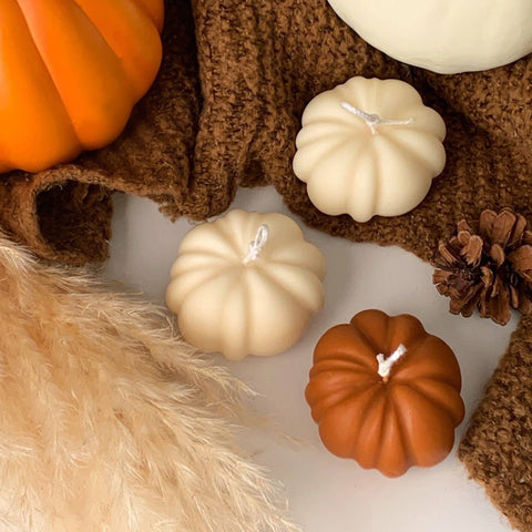 Decorative pumpkins and candles on a textured surface with a brown fabric background