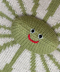 Knitted green character with a red mouth and black eyes on a striped fabric background